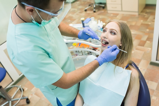 Jovem sentada na cadeira do dentista com a boca aberta no consultório do dentista enquanto faz o exame.