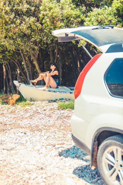 Jovem sentada no barco na praia perto do carro