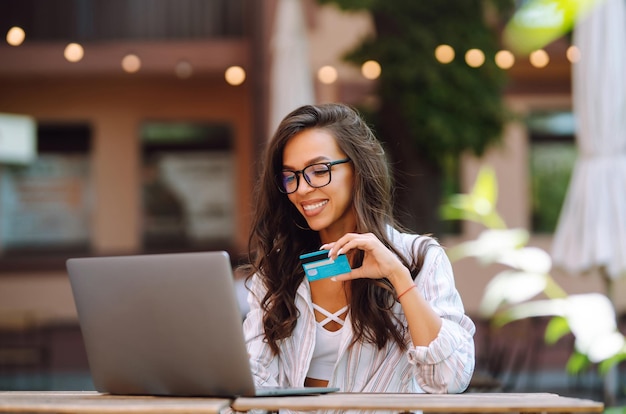 Jovem sentada no café fazendo compras online usando cartão de crédito e laptop Compras online