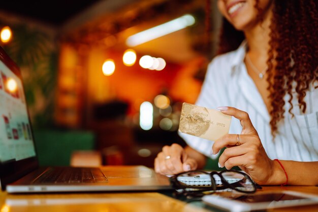 Jovem sentada no café fazendo compras online usando cartão de crédito e laptop Compras online