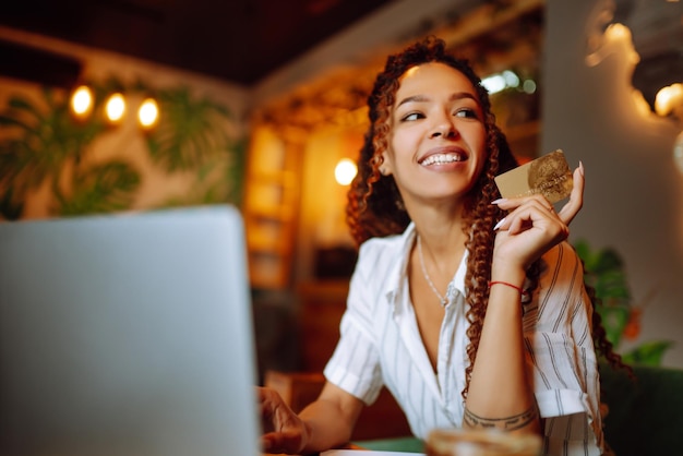 Foto jovem sentada no café fazendo compras online usando cartão de crédito e laptop compras online