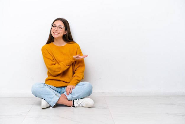 Jovem sentada no chão isolada no fundo branco apresentando uma ideia enquanto olha sorrindo para