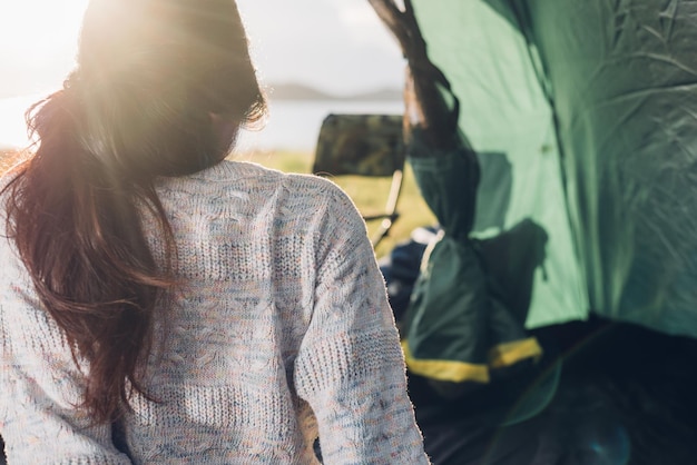 Jovem sentada olhando para fora da barraca de acampamento em viagens de férias ao ar livre no verão