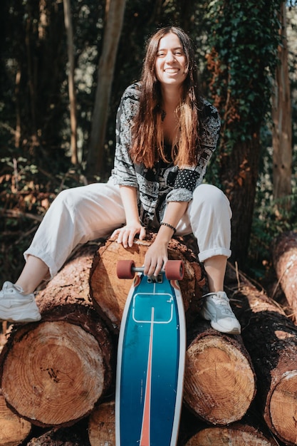 Jovem sentada sobre uma pilha de troncos descansando durante a sessão de longboardmoderno e moderno gen z