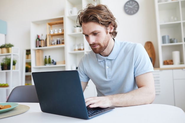 Jovem sentado à mesa e usando o laptop em casa