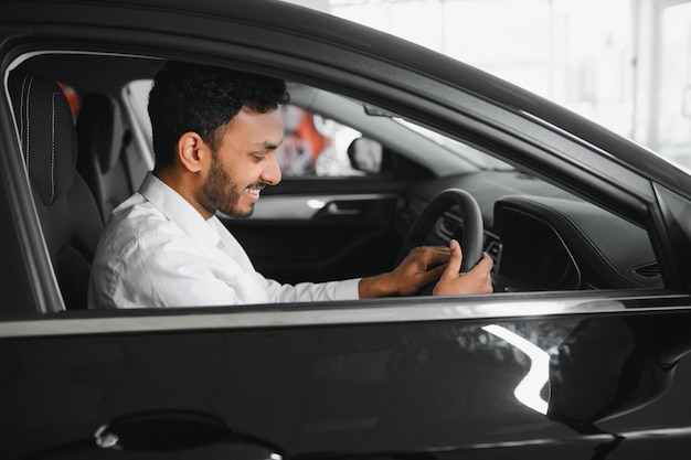 Jovem sentado dentro de um carro novo sorrindo