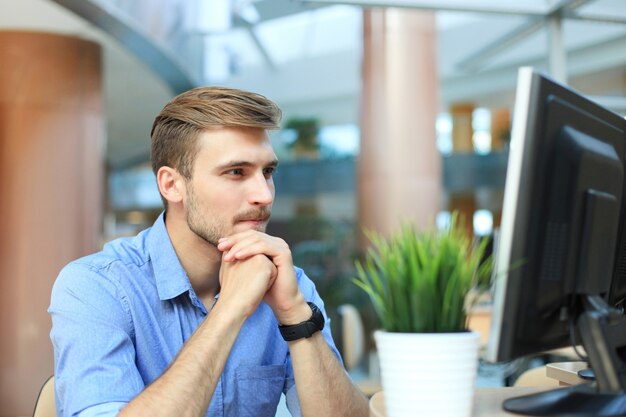 Jovem sentado e olhando para o monitor do computador enquanto trabalhava no escritório.