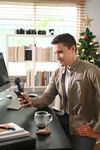 Jovem sentado em frente ao computador e usando o celular