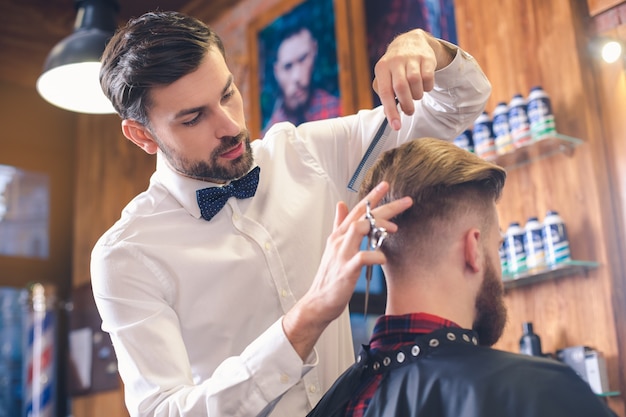 Jovem sentado em uma barbearia enquanto um barbeiro corta o cabelo