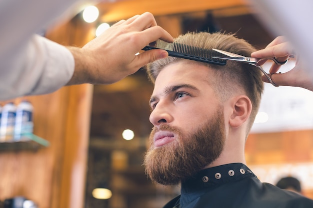 Foto jovem sentado em uma barbearia enquanto um barbeiro corta o cabelo