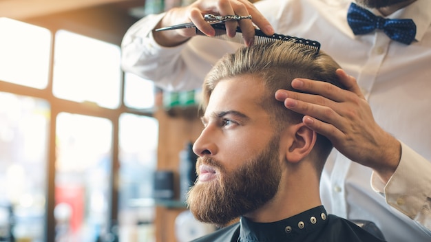 Jovem sentado em uma barbearia enquanto um barbeiro corta o cabelo