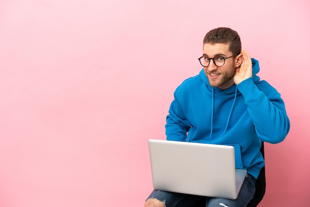 Jovem sentado em uma cadeira com laptop ouvindo algo colocando a mão na orelha