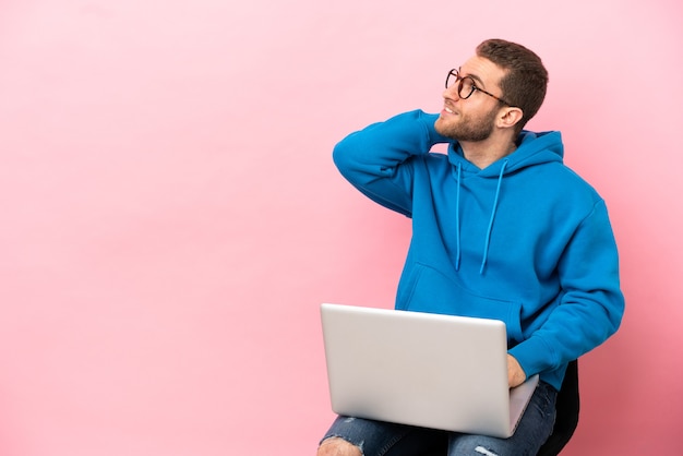 Jovem sentado em uma cadeira com um laptop, pensando em uma ideia