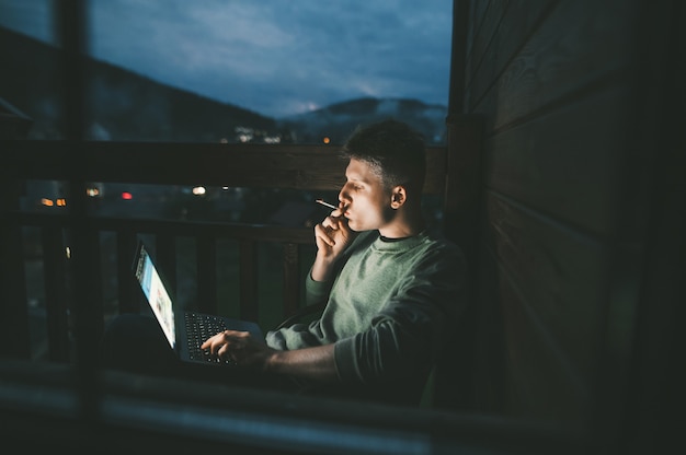 Jovem sentado em uma cadeira em uma varanda usando um laptop