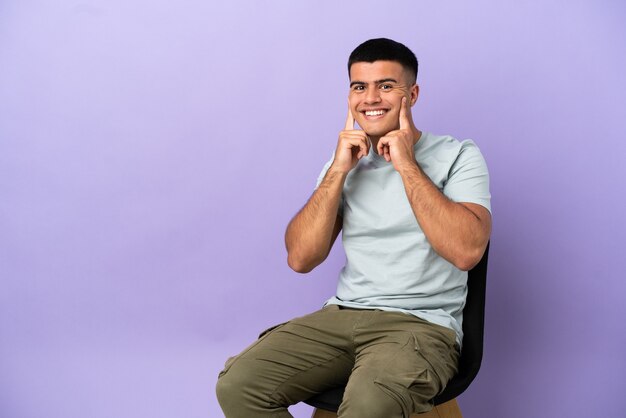 Jovem sentado em uma cadeira sobre um fundo isolado sorrindo com uma expressão feliz e agradável