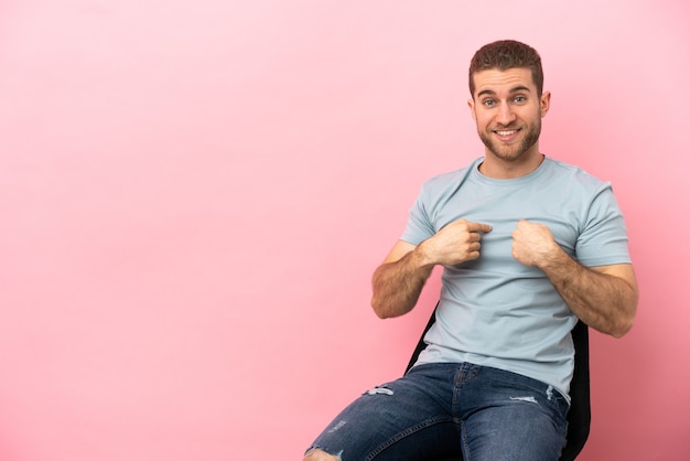 Jovem sentado em uma cadeira sobre um fundo rosa isolado com expressão facial surpresa