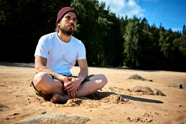 Foto jovem sentado na areia na praia contra as árvores