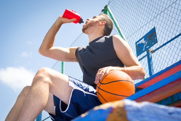 Jovem sentado na arquibancada do campo de basquete