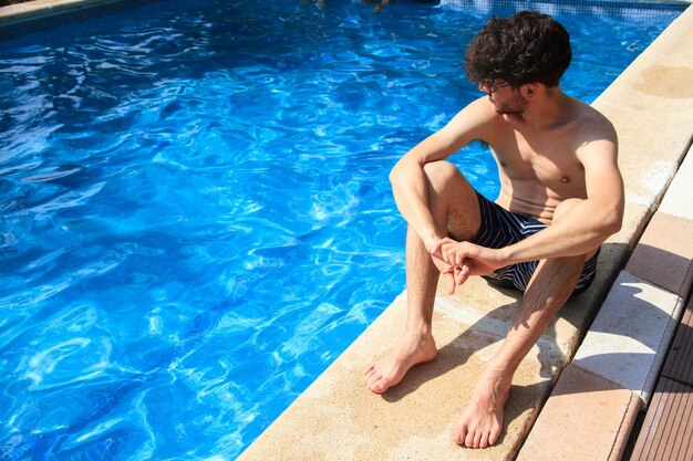 Jovem sentado na beira da piscina