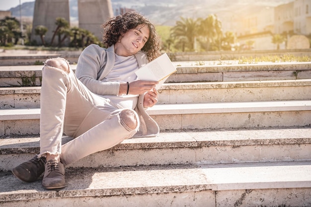 Jovem sentado na escada lendo um livro ao ar livre em uma pausa na cidade