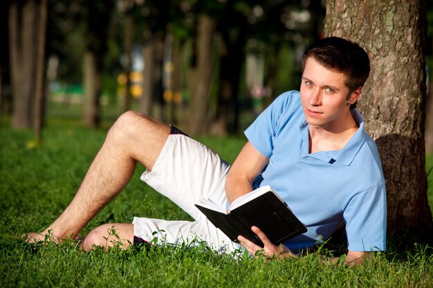 Jovem sentado na grama verde lendo um livro