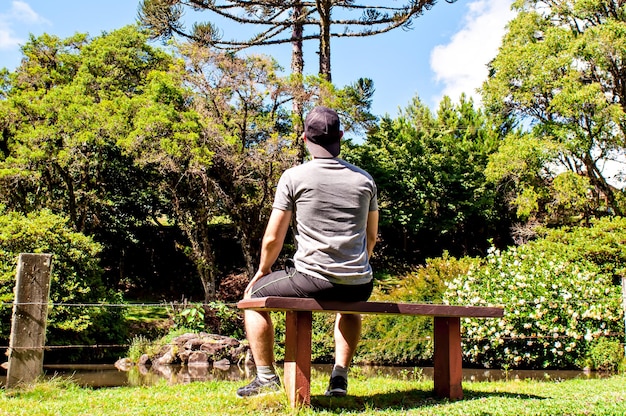 Jovem sentado no banco do jardim observando a natureza