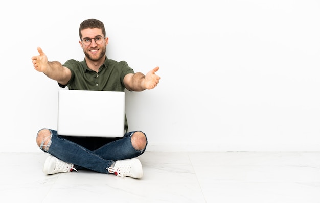 Jovem sentado no chão apresentando e convidando para vir com a mão