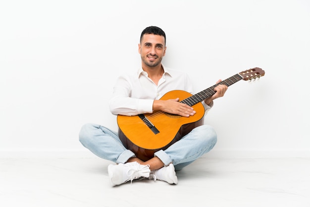 Jovem sentado no chão com guitarra sorrindo muito