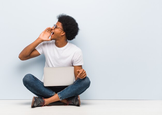 Jovem sentado no chão com um laptop sussurrando fofoca tom