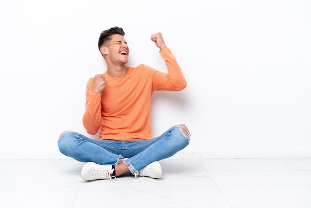 Jovem sentado no chão isolado no fundo branco comemorando uma vitória