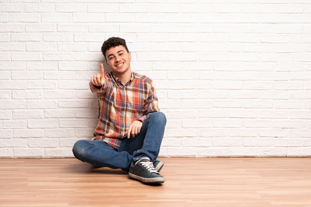 Jovem sentado no chão, mostrando e levantando um dedo