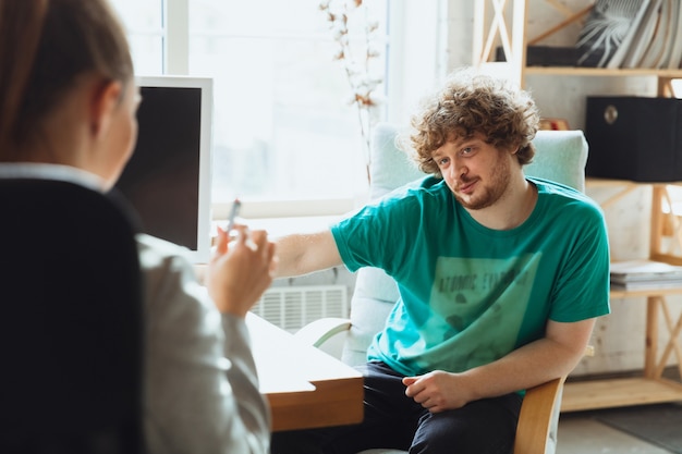 Jovem sentado no escritório durante a entrevista de emprego com uma funcionária, chefe ou gerente de rh