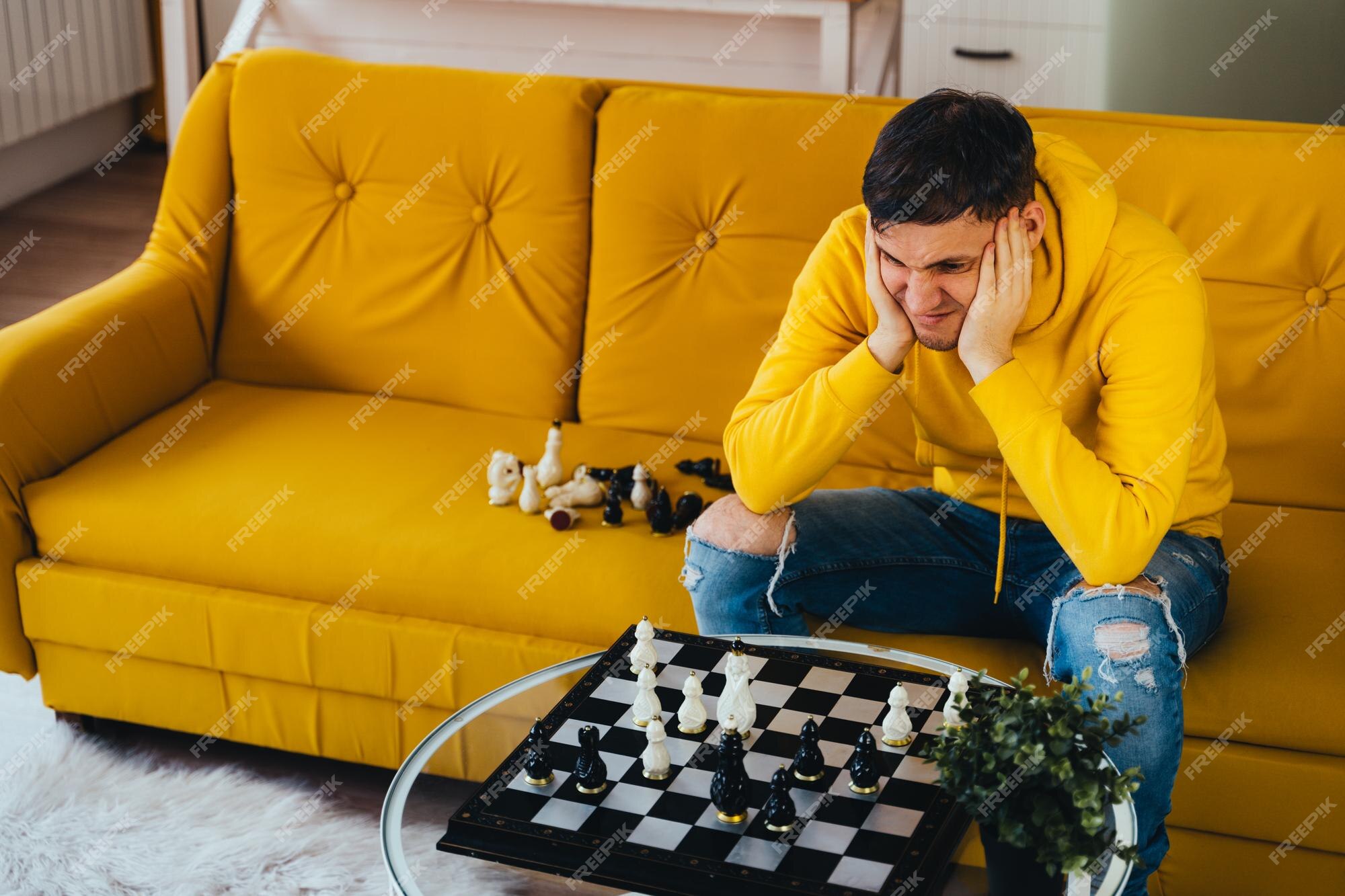 Jovem sentado no sofá amarelo e jogando xadrez na sala macho jogando no jogo  de tabuleiro lógico consigo mesmo