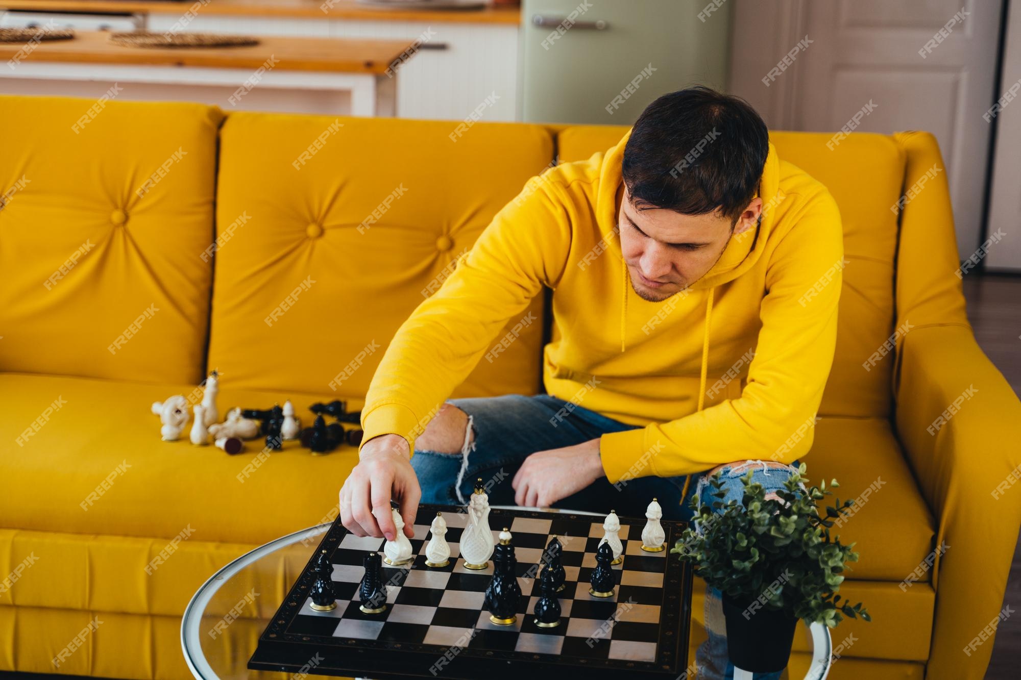 Jovem sentado no sofá amarelo e jogando xadrez na sala macho jogando no jogo  de tabuleiro lógico consigo mesmo