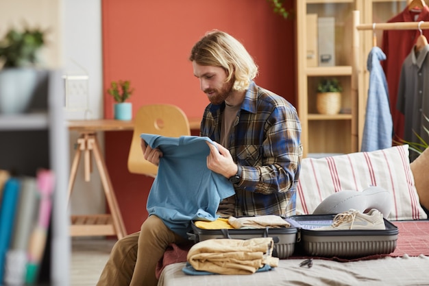 Jovem sentado no sofá arrumando roupas na mala e se preparando para as férias