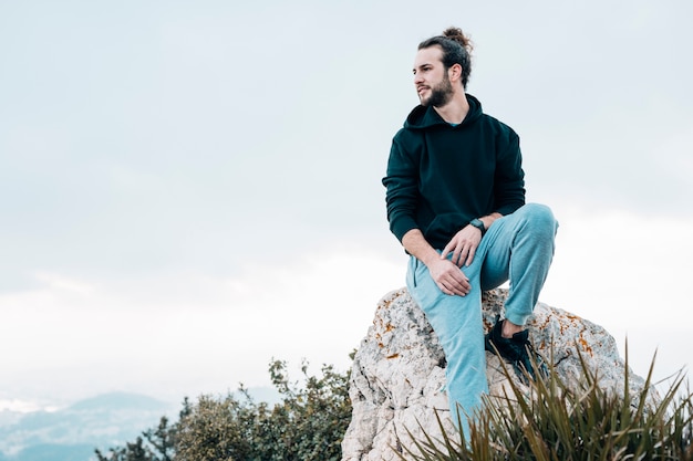 Jovem sentado no topo da rocha, olhando a vista