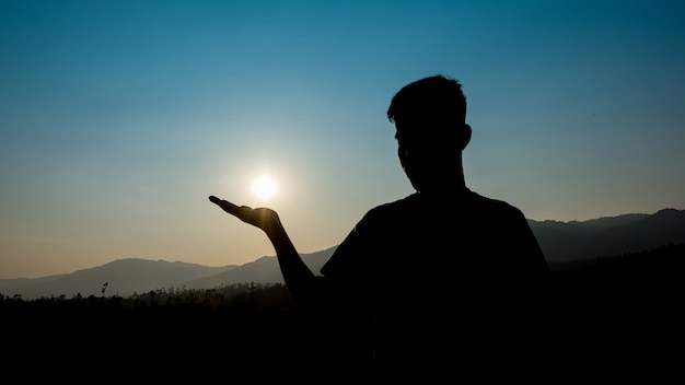 Jovem sentado sozinho durante o pôr do sol. Silhueta de um jovem ao ar livre.