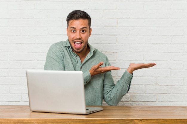 Jovem sentado trabalhando com seu laptop animado segurando algo na palma da mão