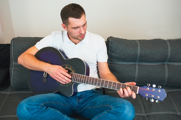 Jovem sente-se na sala tocando violão. Aprendendo sozinho. Segure os dedos nas cordas e toque. Músico na foto.