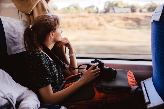 Jovem sente-se viajando de trem. sente-se sozinho na janela e olhe para ela. fotógrafo feminino tem tempo de férias ou feriados. viajar para o exterior ou para dentro do país.