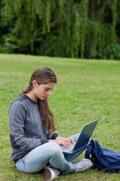 Jovem séria digitando em seu laptop enquanto está sentada de pernas cruzadas