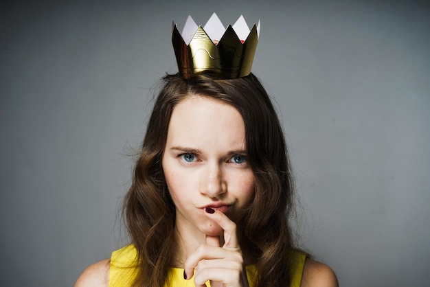 Jovem séria em um vestido amarelo pensa em algo, na cabeça uma coroa de ouro