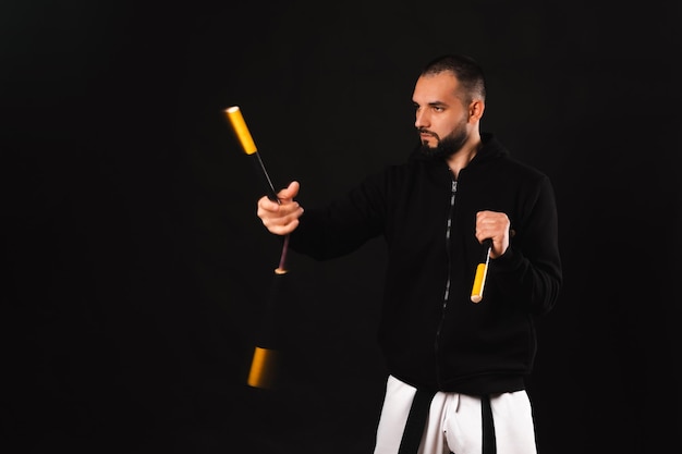 Jovem sério executa um movimento de arte marcial nunchaku sobre fundo escuro