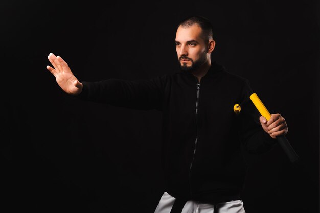 Jovem sério executa um movimento de arte marcial nunchaku sobre fundo escuro