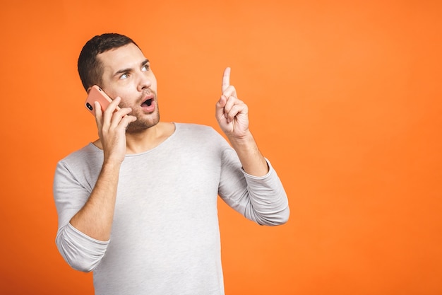 Jovem sério falando no celular isolado em um fundo laranja