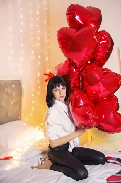 jovem sexy no quarto com balões em forma de coração no dia dos namorados na cama
