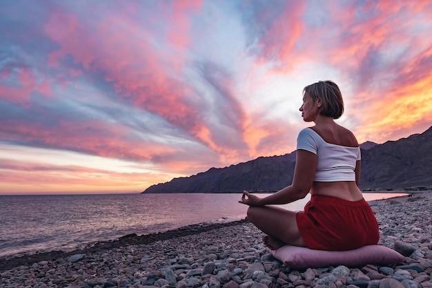 Foto jovem shilhouette em posição de meditação na praia contra o céu ao pôr-do-sol