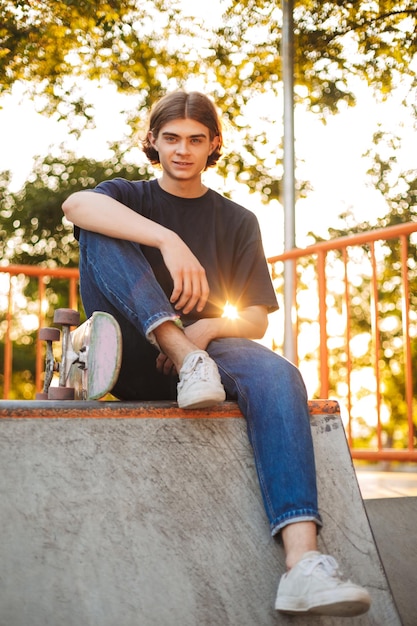 Jovem skatista sorridente feliz olhando na câmera com skate no moderno parque de skate