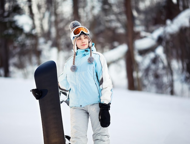 Jovem snowboarder feminina em pé na pista de esqui segurando seu snowboard