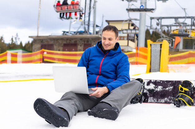 Jovem snowboarder usando laptop na montanha de neve. Neve branca e céu azul. Copie o espaço para anúncio.